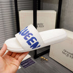 Alexander McQueen white slide sandals with blue logo strap, angled view