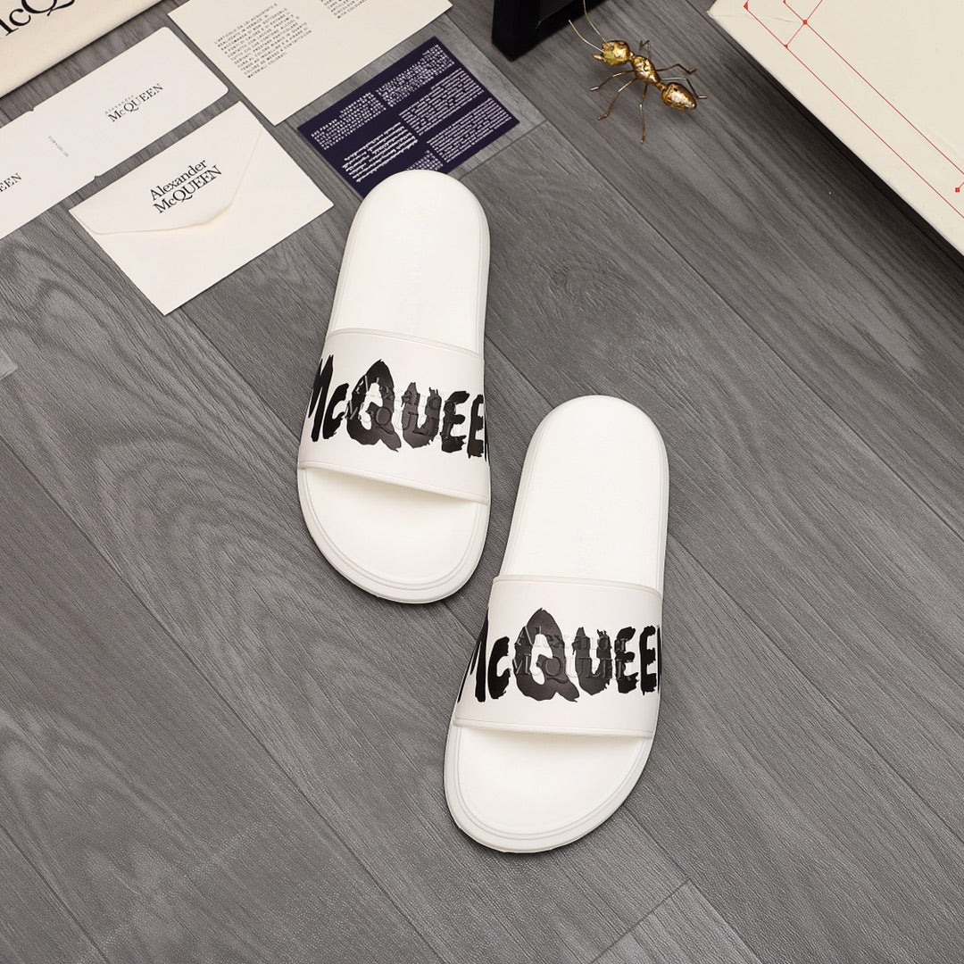Pair of white slide sandals with black McQUEEN text on straps