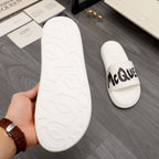 White slide sandals with textured outsole tread and McQUEEN logo on strap