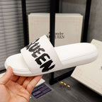 White slide sandals with black McQUEEN logo on the front strap
