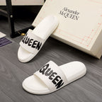 White slide sandals with black McQUEEN graphic across the strap