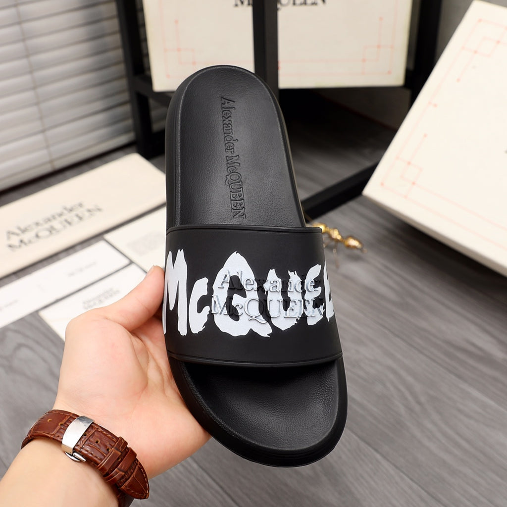 Black Alexander McQueen slide sandal held in hand, white McQueen logo on strap.