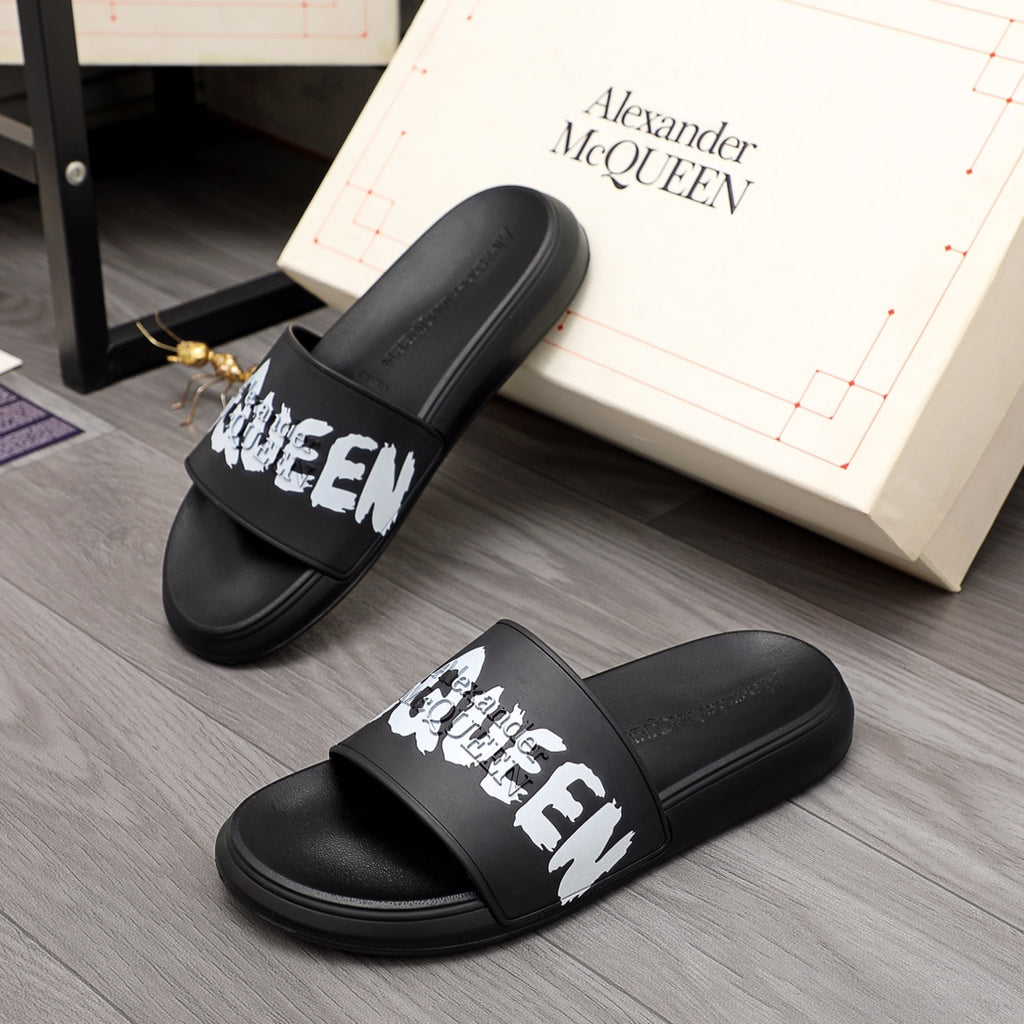 Black slide sandals with wide strap and white McQueen graphic, Alexander McQueen branding.