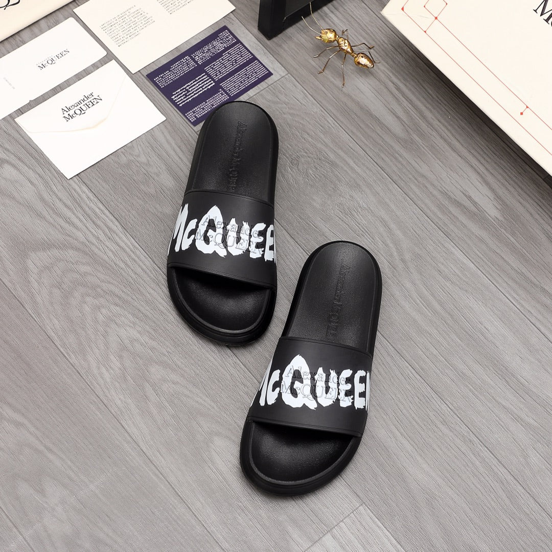 Pair of black McQueen slide sandals with white logo on front strap.