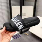 Black slide sandal with white McQueen graphic strap, shown from side angle.