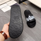 Rubber outsole view of black slide sandals with textured tread, side shows white logo strap.