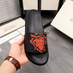 Black slide sandal with orange graphic logo on front strap, held in hand