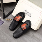 Black Alexander McQueen slide sandals with orange graphic logo, on display
