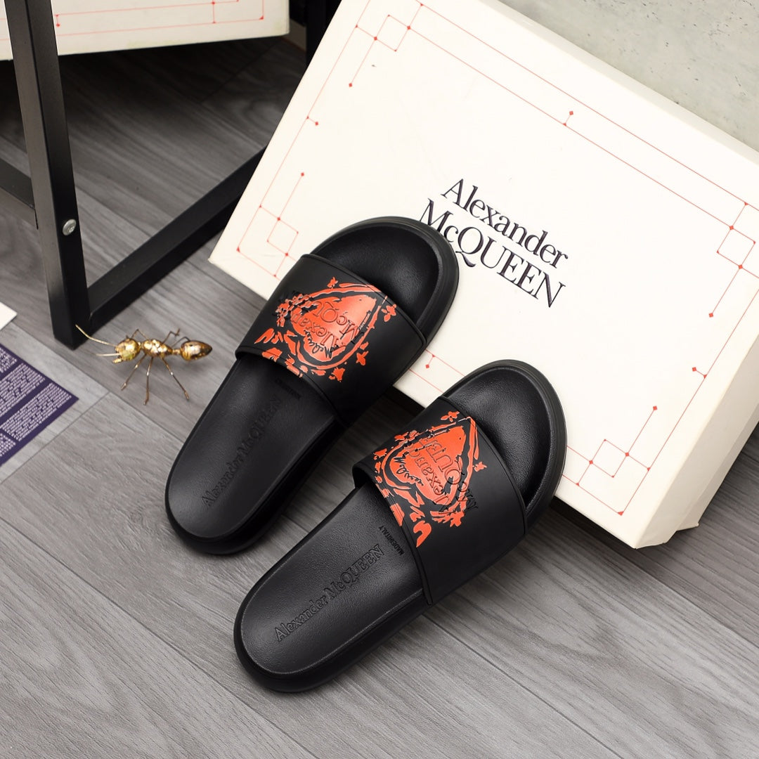 Black Alexander McQueen slide sandals with orange graphic logo, on display