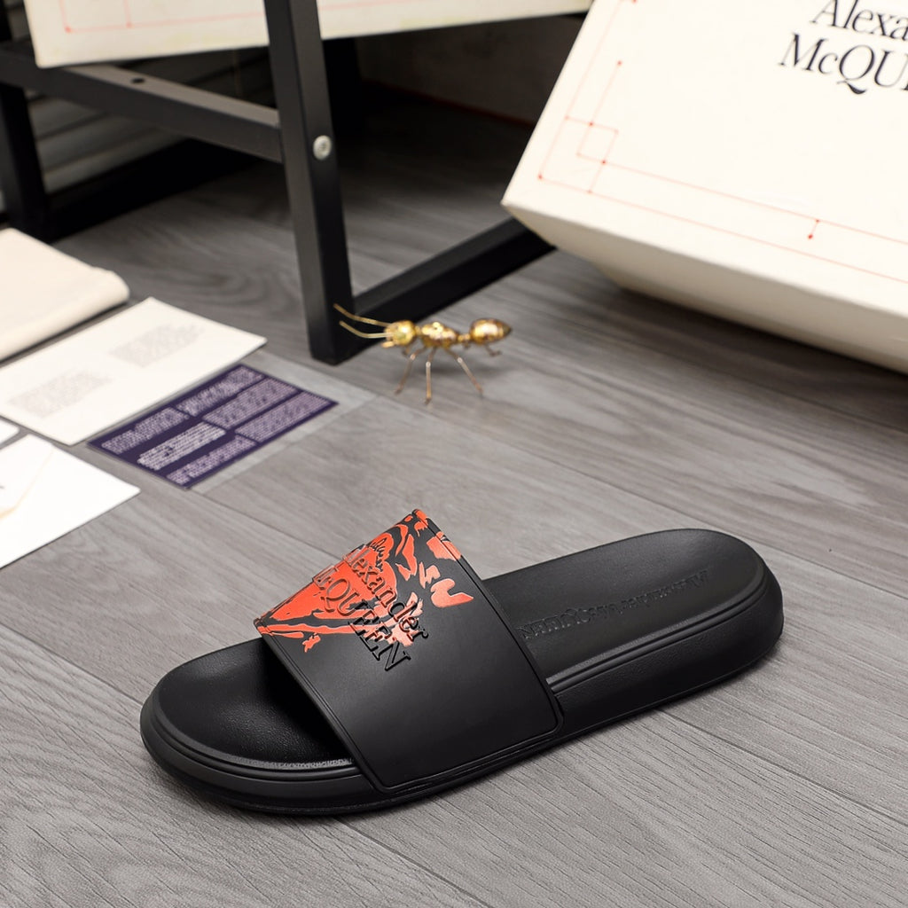 Black slide sandal with orange graphic logo on front strap