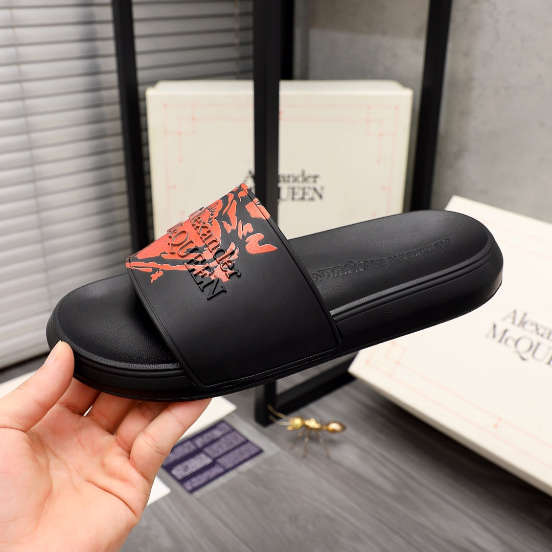 Black slide sandal with orange graphic logo on front strap, side view