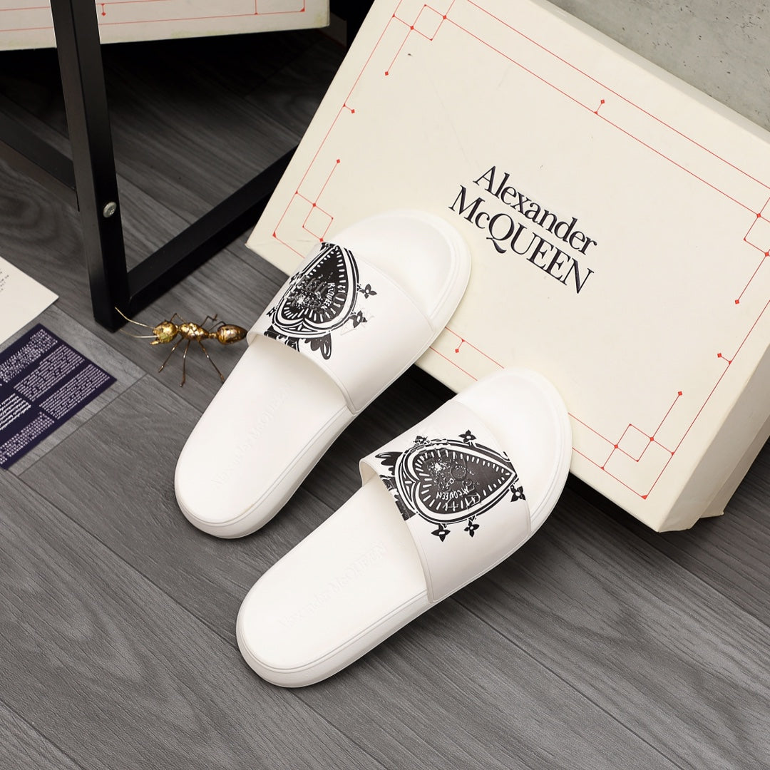 White slide sandals with black graphic emblem, shown near the branded box