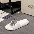 White slide sandals featuring a black emblem print on the front strap