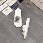 White slide sandals with black emblem print on the strap, pair view