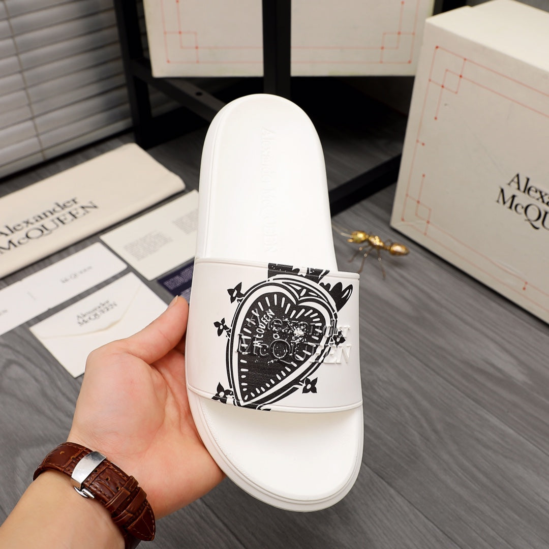 White slide sandal with black patterned emblem on the front strap, shown in hand