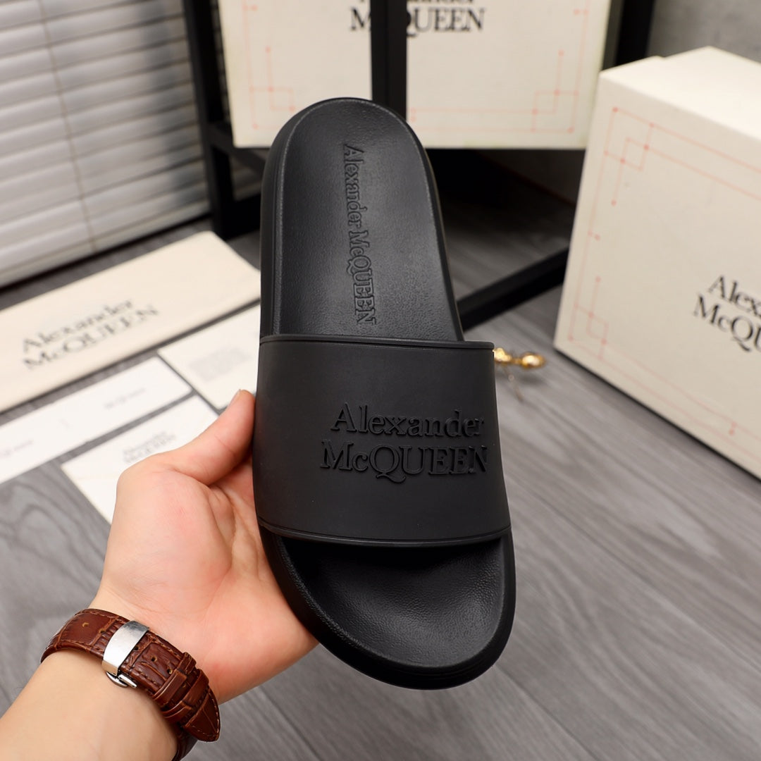 Black slide sandal held in hand, wide strap with Alexander McQUEEN logo on footbed