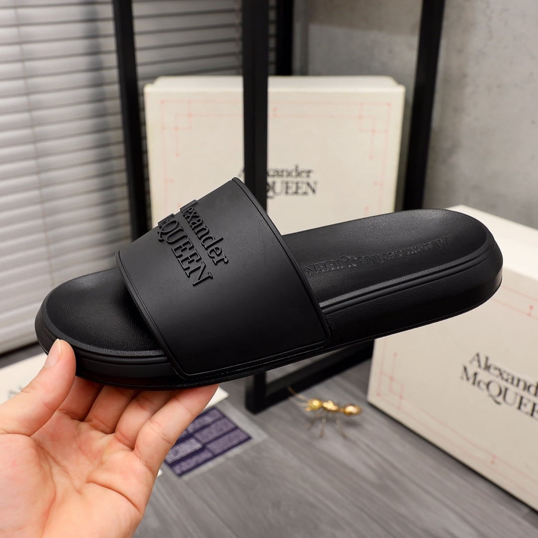 Black slide sandals with wide strap and embossed Alexander McQUEEN branding, close view