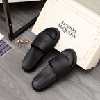 Black slide sandals pair with wide straps and Alexander McQUEEN branding on floor
