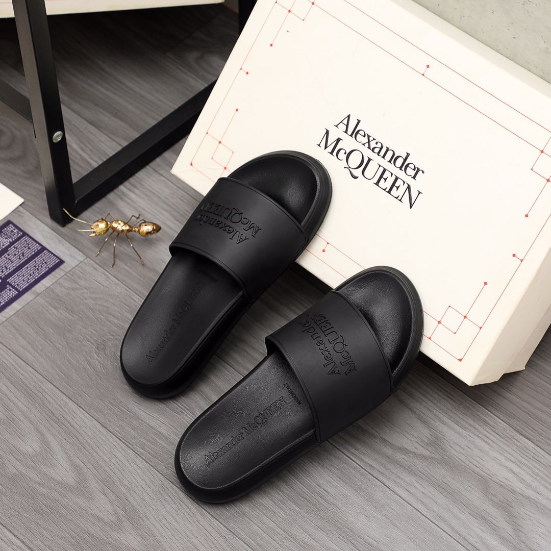 Black slide sandals pair with wide straps and Alexander McQUEEN branding on floor