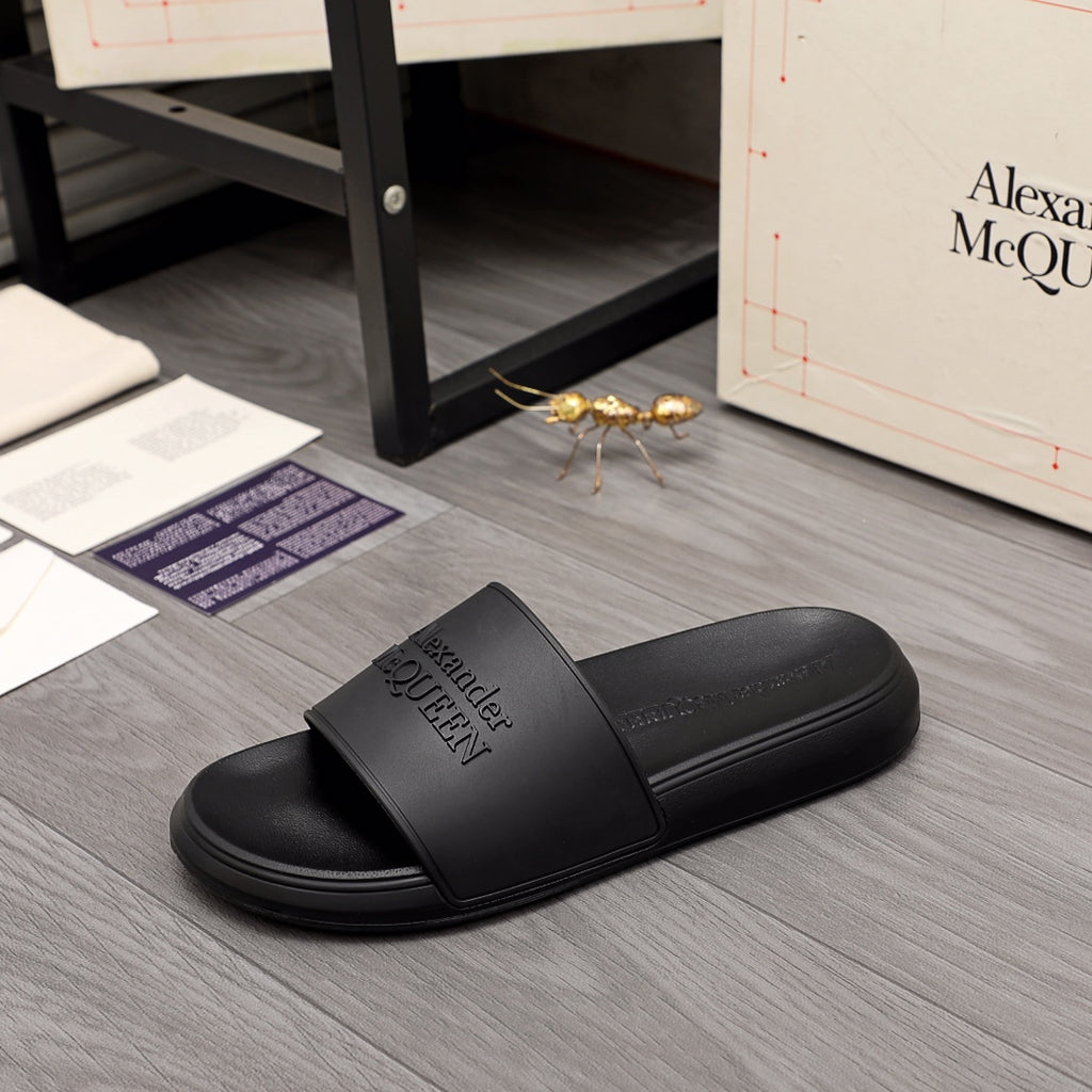 Black slide sandals with wide strap and embossed Alexander McQUEEN branding, side view