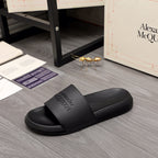 Black slide sandals with wide strap and embossed Alexander McQUEEN branding, side view