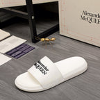 White slide sandal with logo strap, laid on floor near shoe box