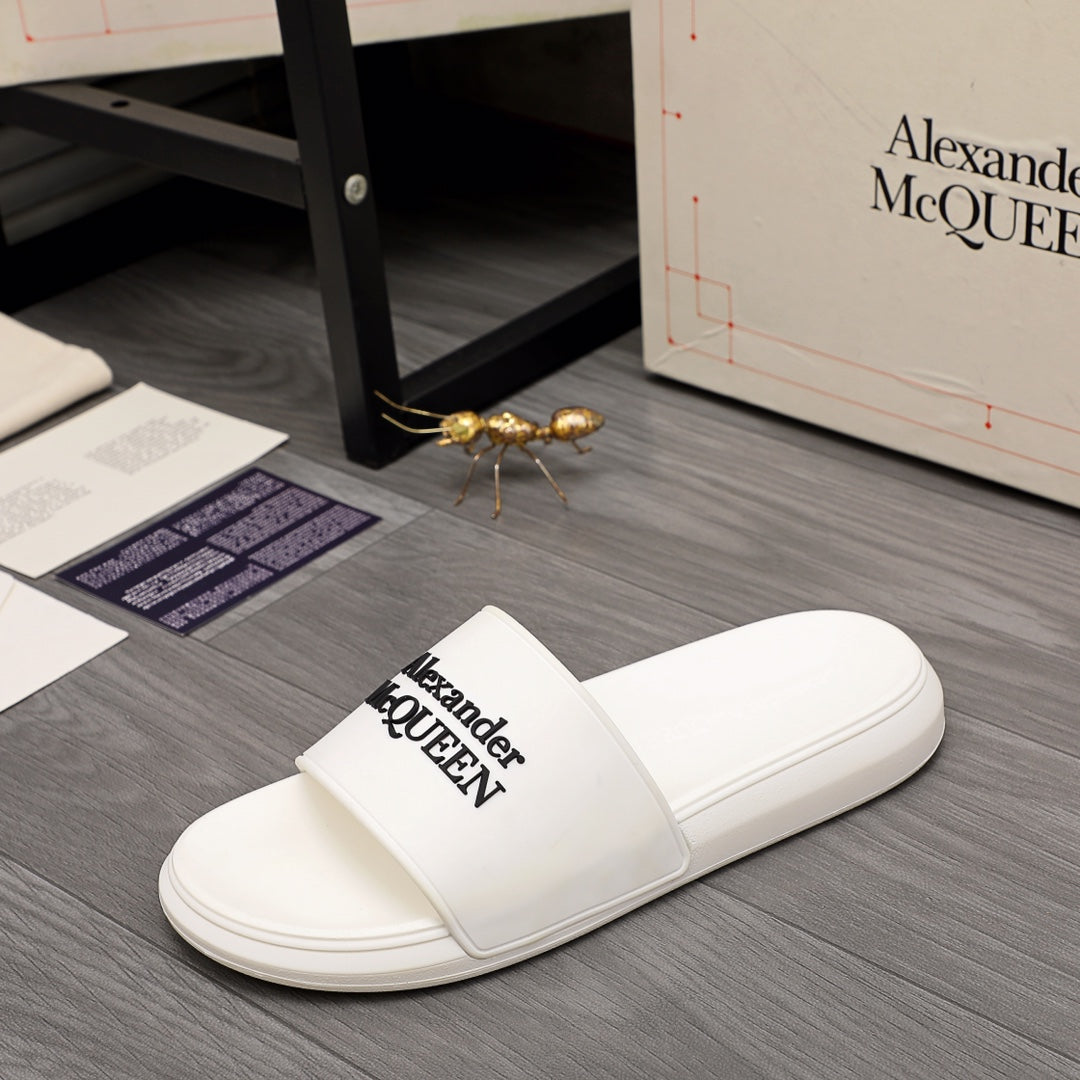White slide sandal with logo strap, laid on floor near shoe box