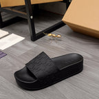 Black slide sandal with wide strap, textured geometric embossing, and flat sole