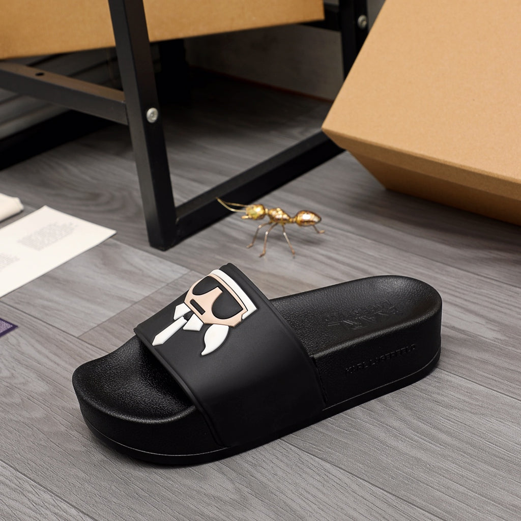 Black slide sandals with large graphic logo on front strap, pair on floor