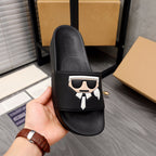 Black slide sandals held in hand, graphic face emblem on front strap