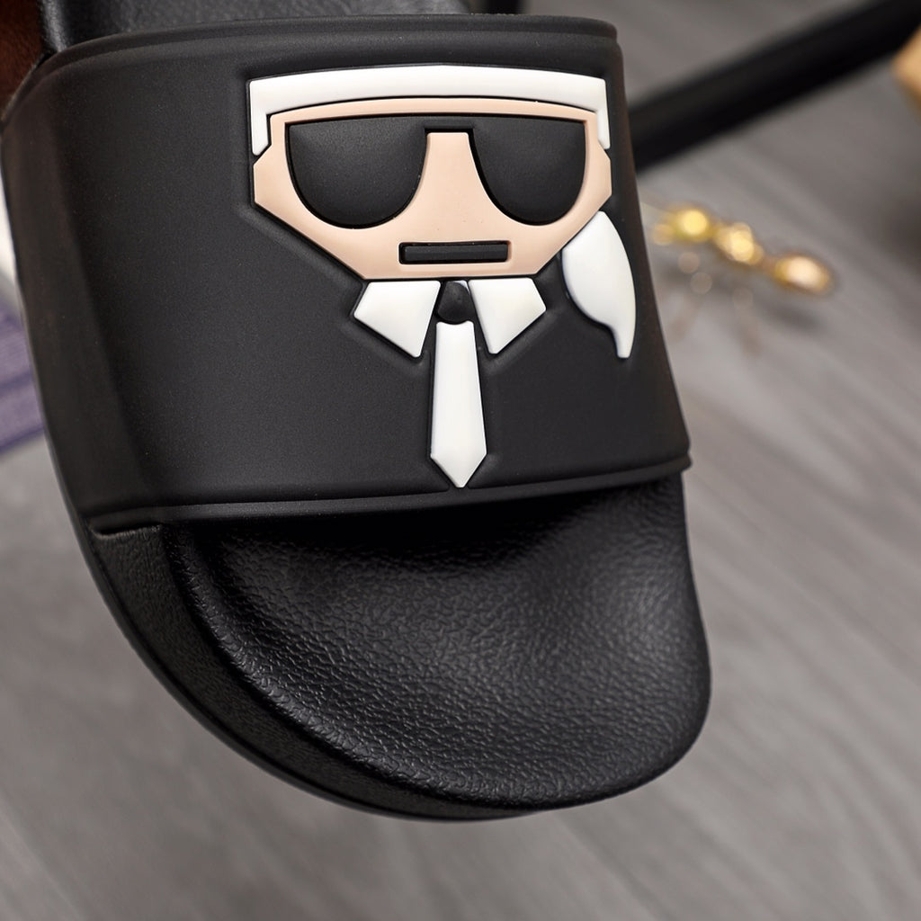 Black slide sandals close-up: graphic face emblem on front strap