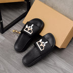Black slide sandals pair with graphic face emblem on front straps