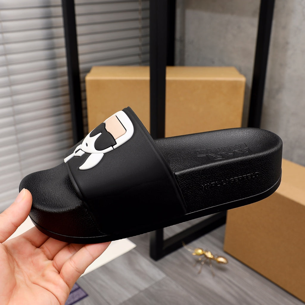 Black slide sandal shown in hand, with white cartoon graphic on the strap