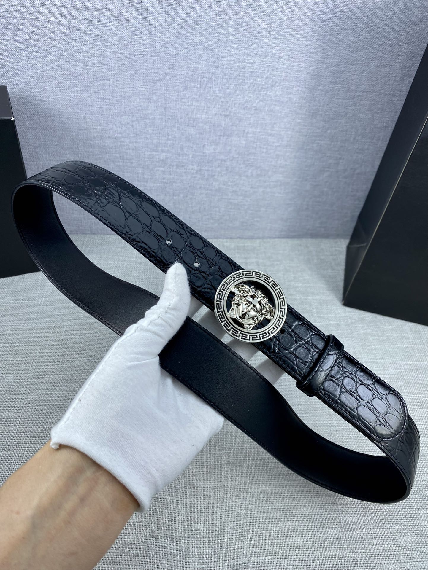Black embossed leather belt with round Versace medallion buckle and curved strap