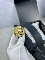 Black leather belt with gold Medusa medallion buckle held upright by a strap.