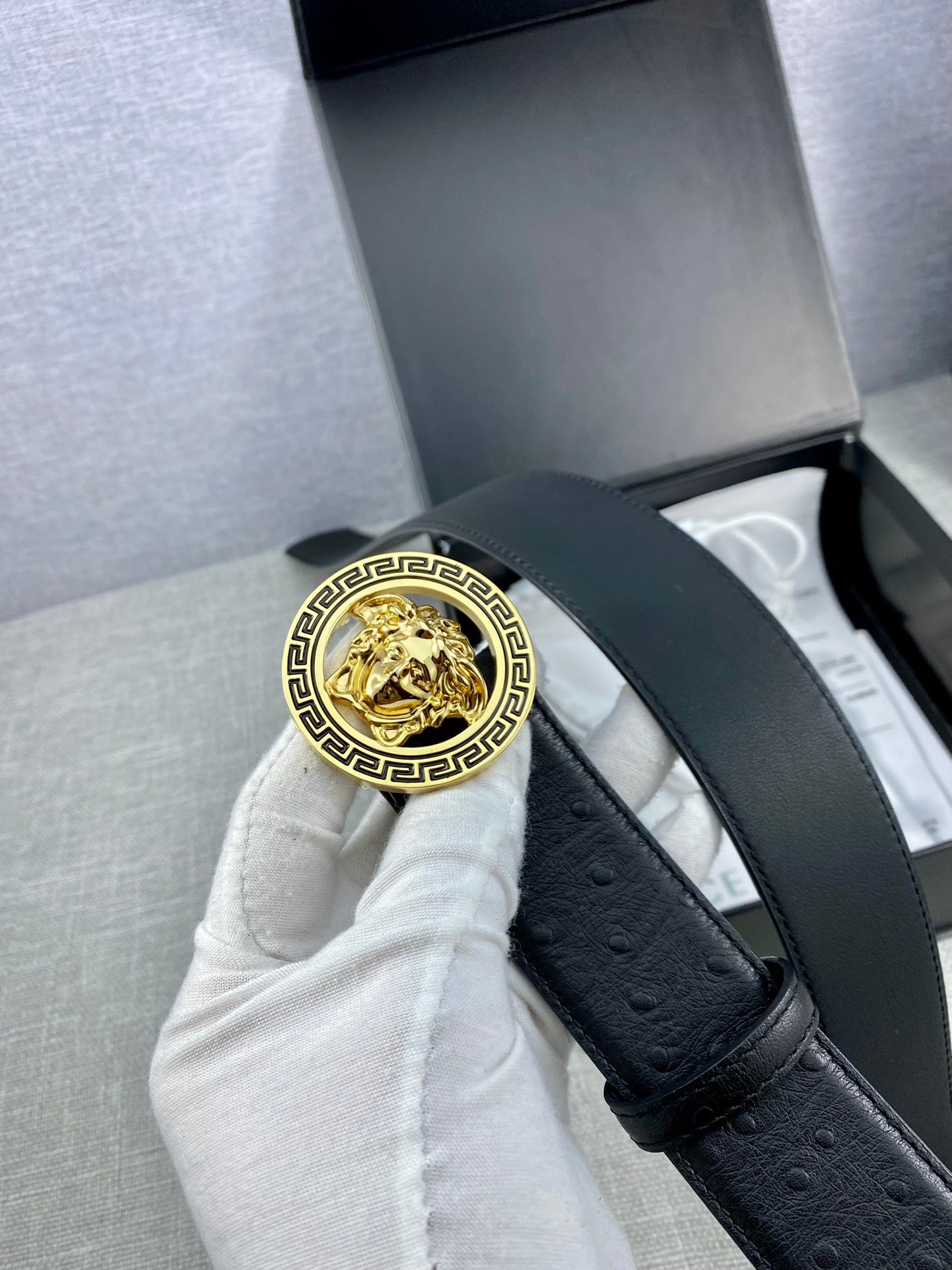 Black leather belt with gold Medusa medallion buckle held upright by a strap.