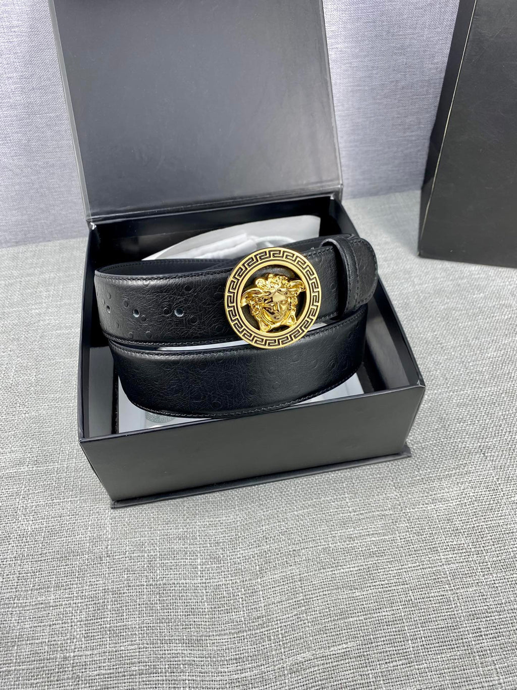Black leather belt with gold Medusa buckle, coiled inside a gift box.