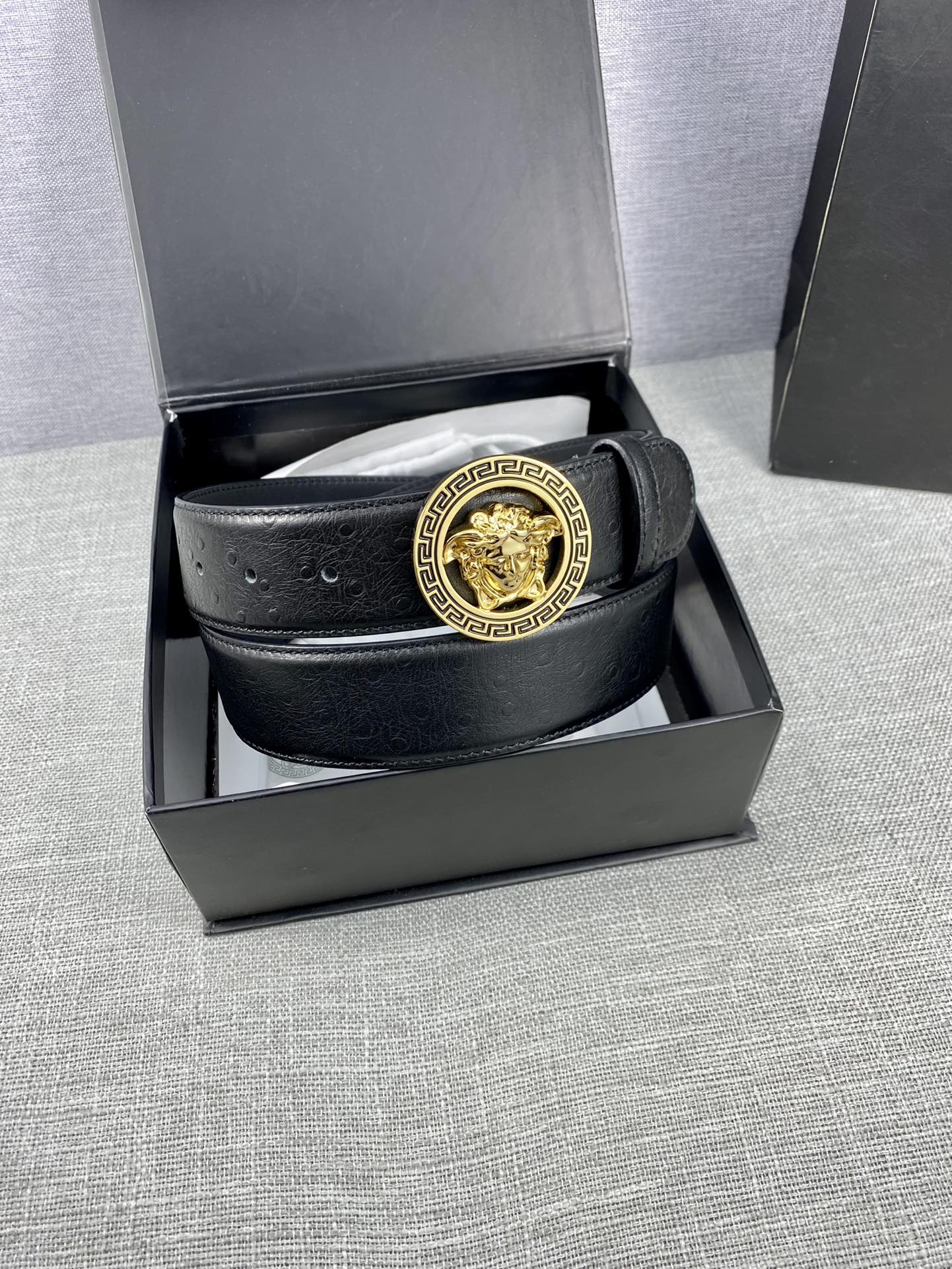 Black leather belt with gold Medusa buckle, coiled inside a gift box.