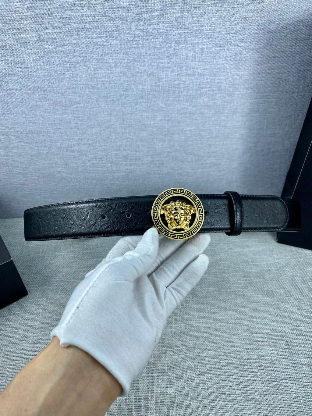 Black leather Versace belt with gold Medusa buckle on an adjustable strap.