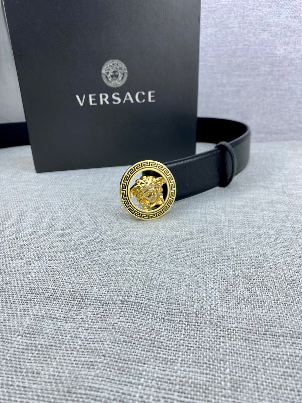 Black leather Versace belt with gold Medusa buckle near a Versace gift box.