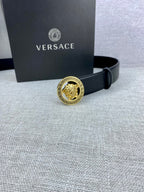 Black leather Versace belt with gold Medusa buckle near a Versace gift box.