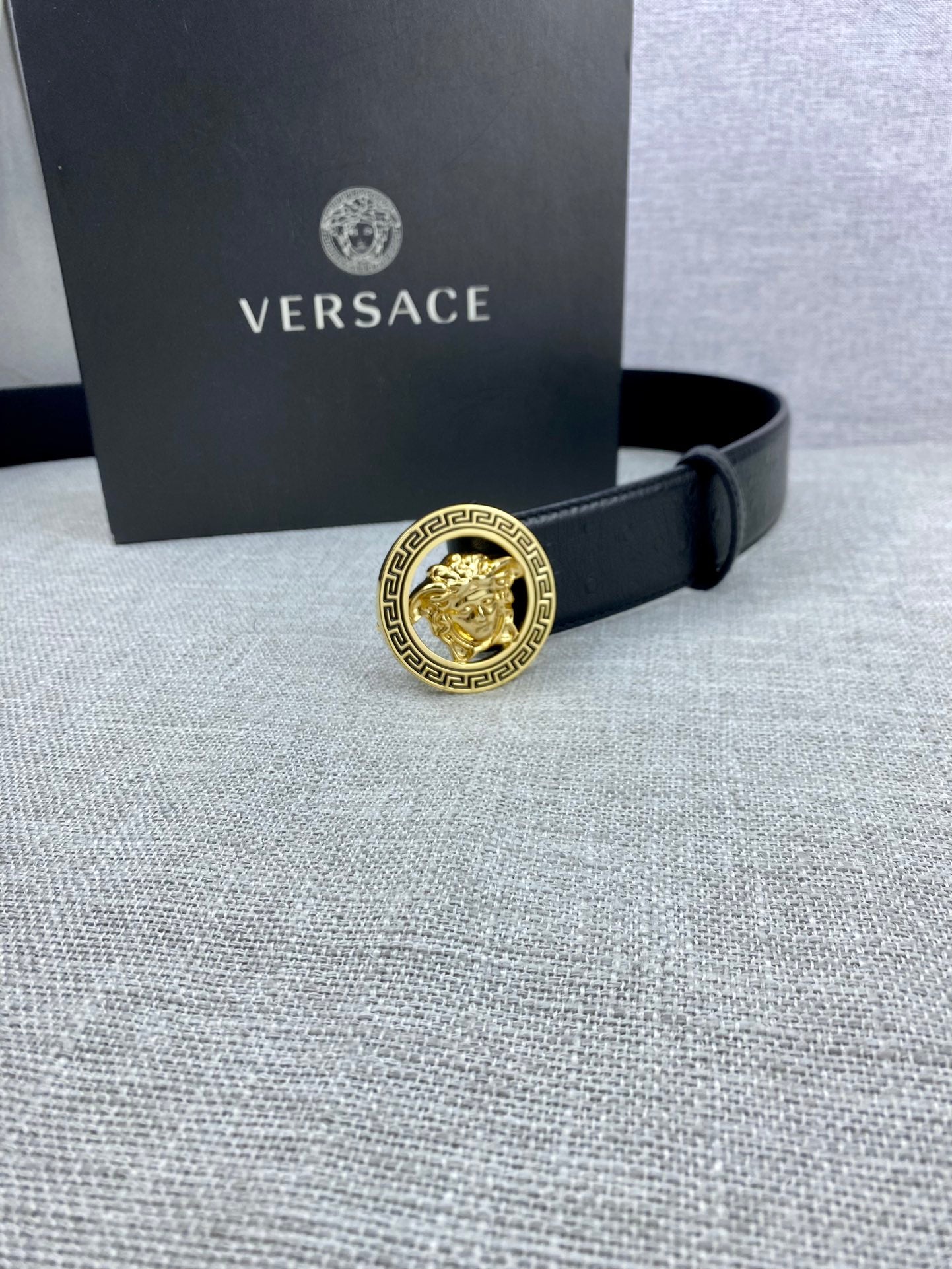 Black leather Versace belt with gold Medusa buckle near a Versace gift box.