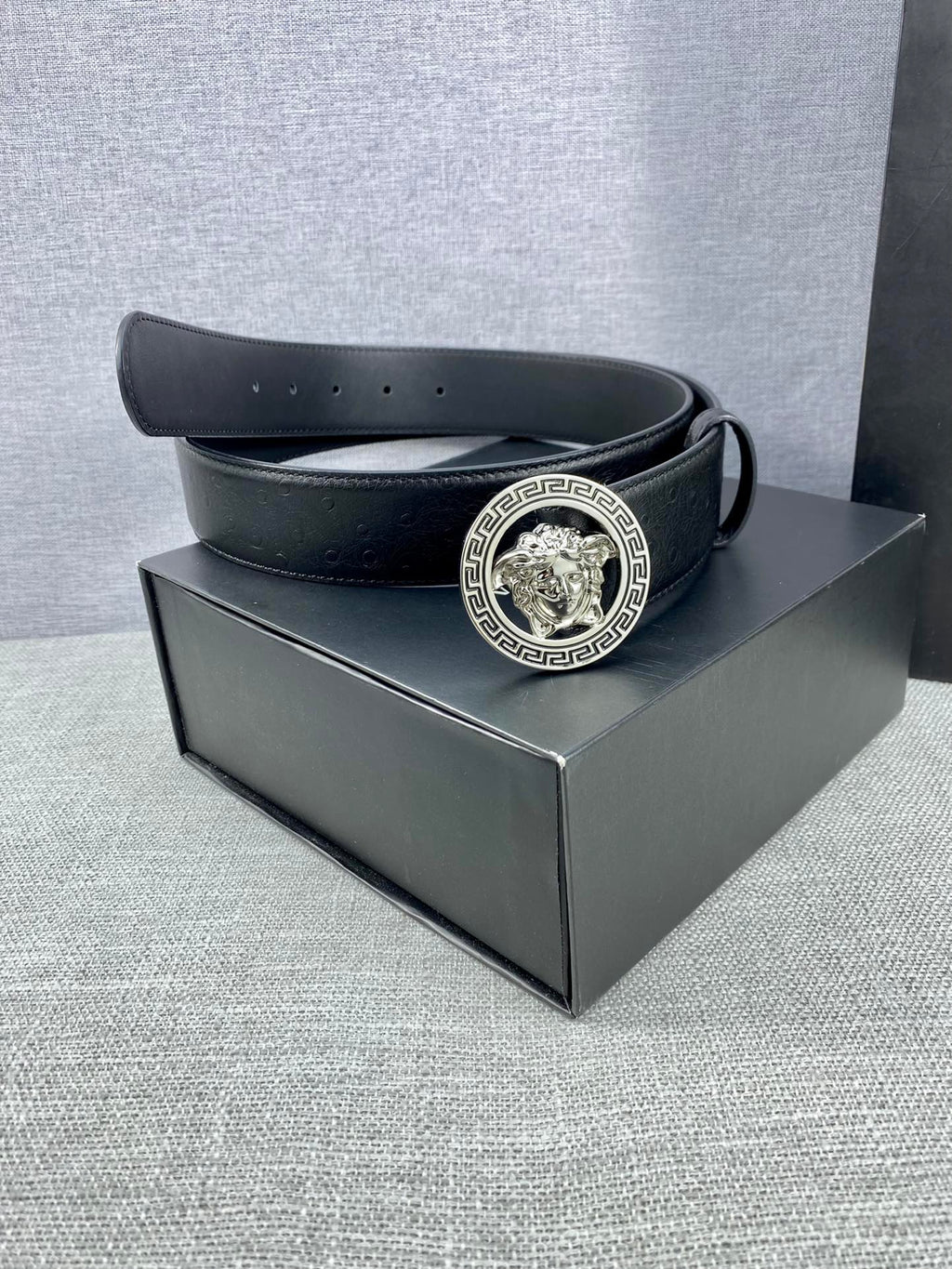 Black leather belt with gold Medusa buckle resting on a box.
