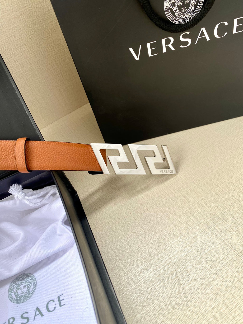 Versace belt with tan leather strap and gold logo buckle, close-up