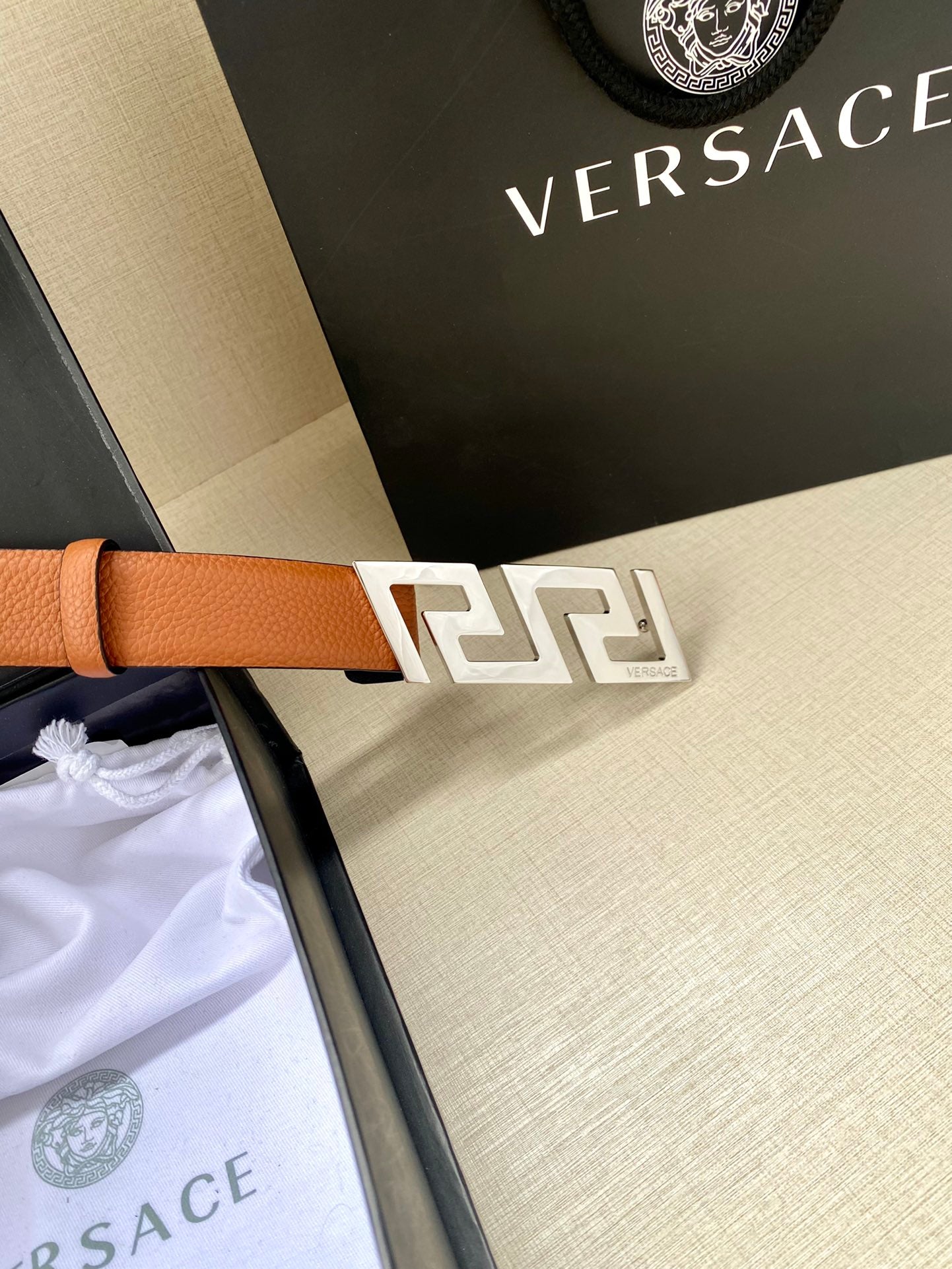 Versace belt with tan leather strap and gold logo buckle, close-up