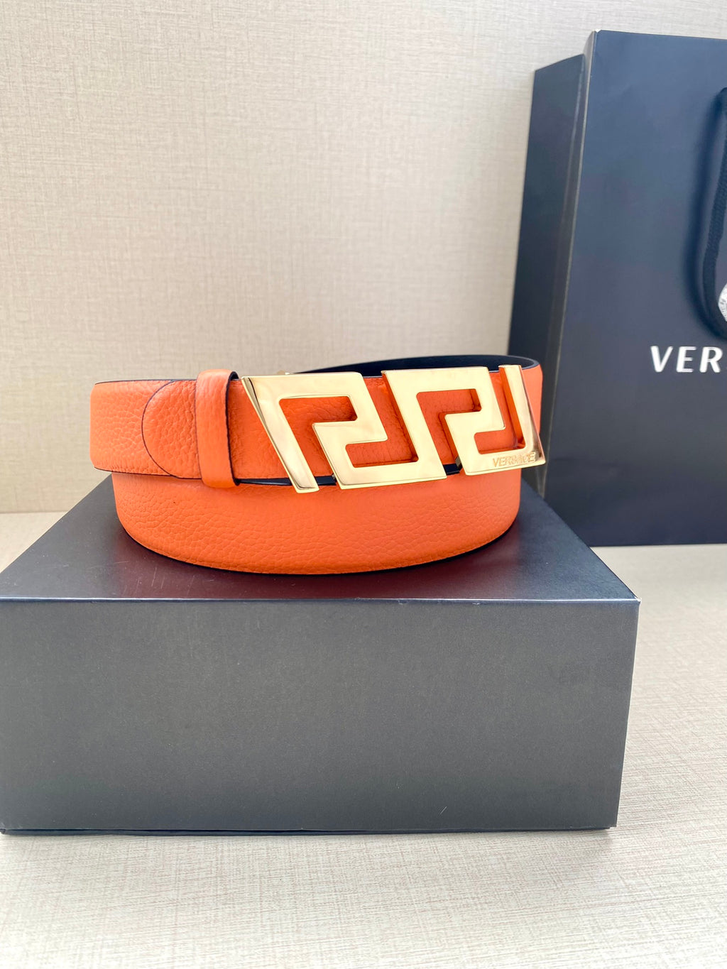 Orange leather belt with gold-tone Greca buckle and logo crest plate.