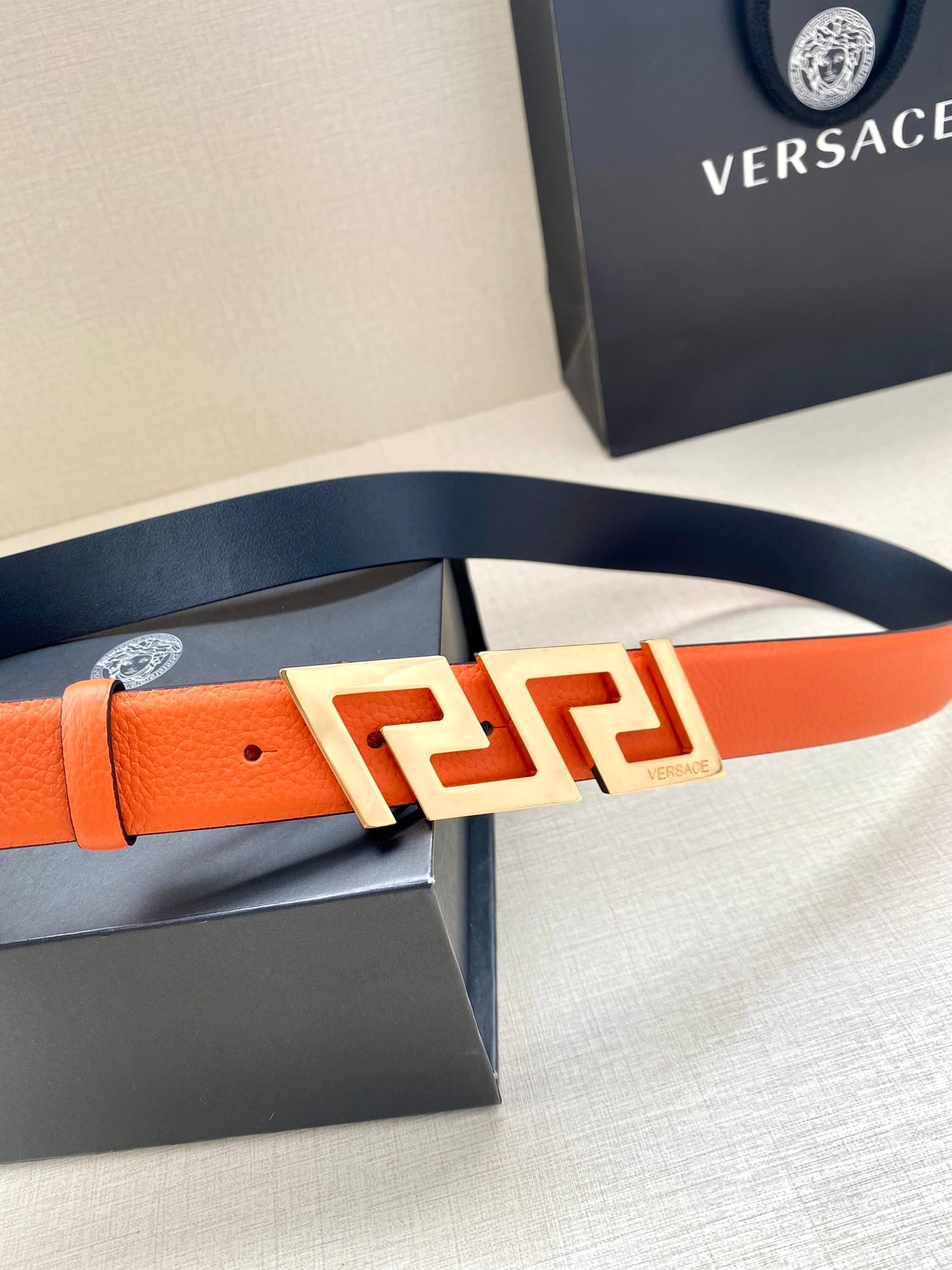 Orange leather belt with gold-tone Greca buckle, partially unboxed.