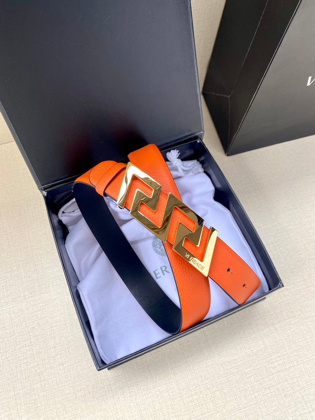 Orange leather belt with gold-tone Greca buckle, shown in display box.