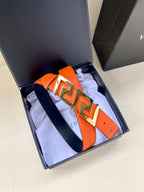 Orange leather belt with gold-tone Greca buckle, shown in display box.