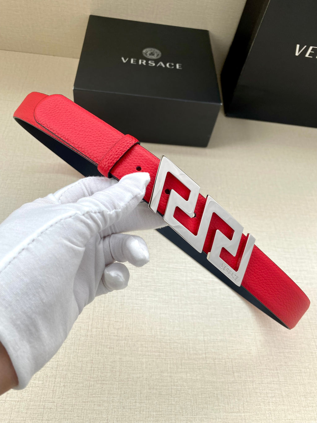 Versace red belt with silver FF buckle, held in a hand